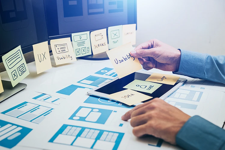 Hände einer Person, die Post-Its und Notizen mit ersten Wireframe-Entwürfen sortiert und durcharbeitet